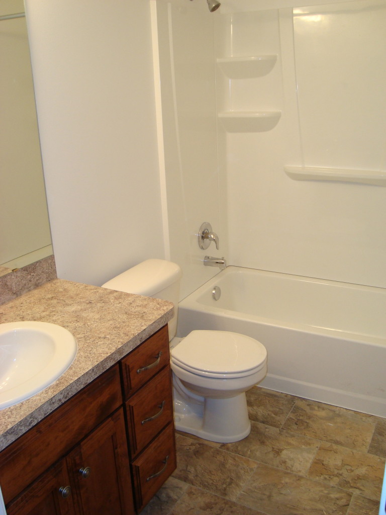 Bathroom picture showing part of sink with cherrywood cabinets underneath, toinlet and shower/bath with built in shower shelves.